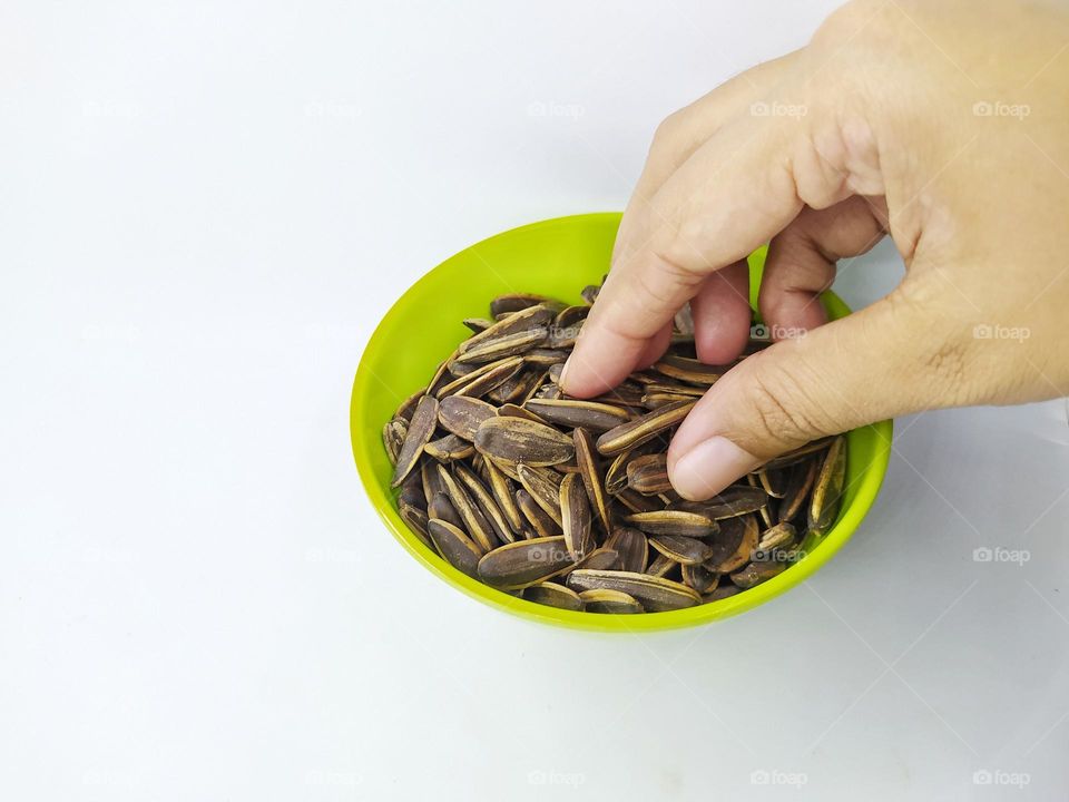 Hand taking some sunflower seeds in a green bowl isolated on white background.