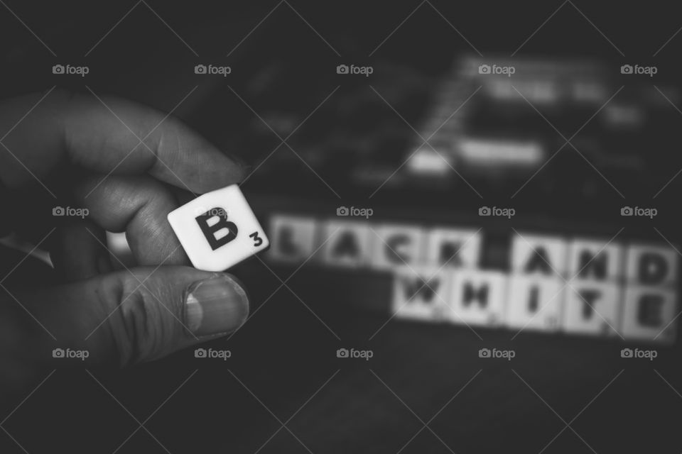 A black and white portrait of a person playing scrabble and holding the letter b. on hij board are the words black and white ready but the b was still missing.