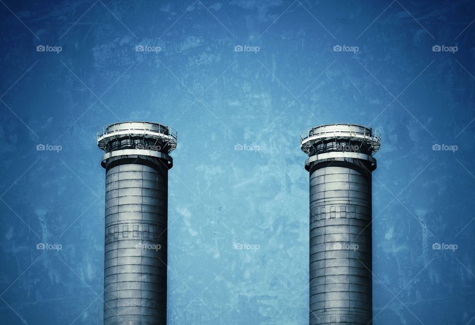 A pair of industrial chimneys against a blue sky.