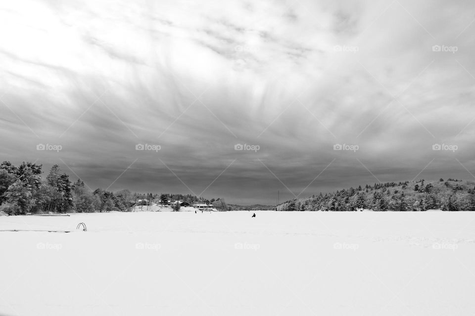 Storm on it’s way with beautiful feather like clouds above snow covered frozen lake where people are ice fishing on a cold winter day, b&w