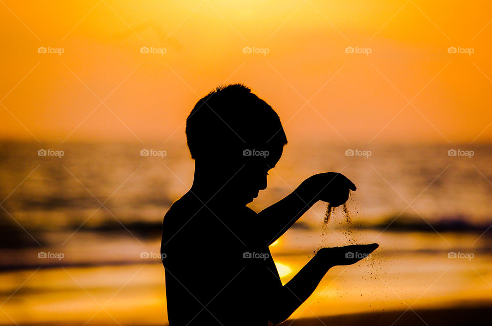 Silueta niño jugando con la arena en la orilla de la playa, tonos cálidos