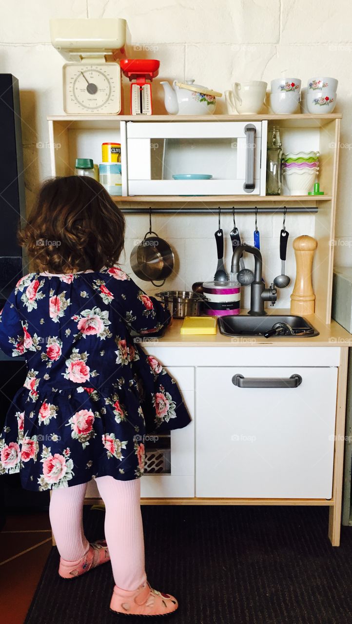 Small girl child with curly hair and floral rose dress cooking up a storm in the kitchen. 