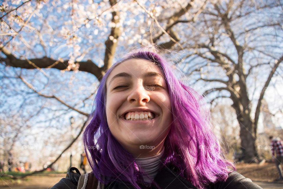 A young woman with purple hair & no makeup proudly giving a big genuine smile for the camera