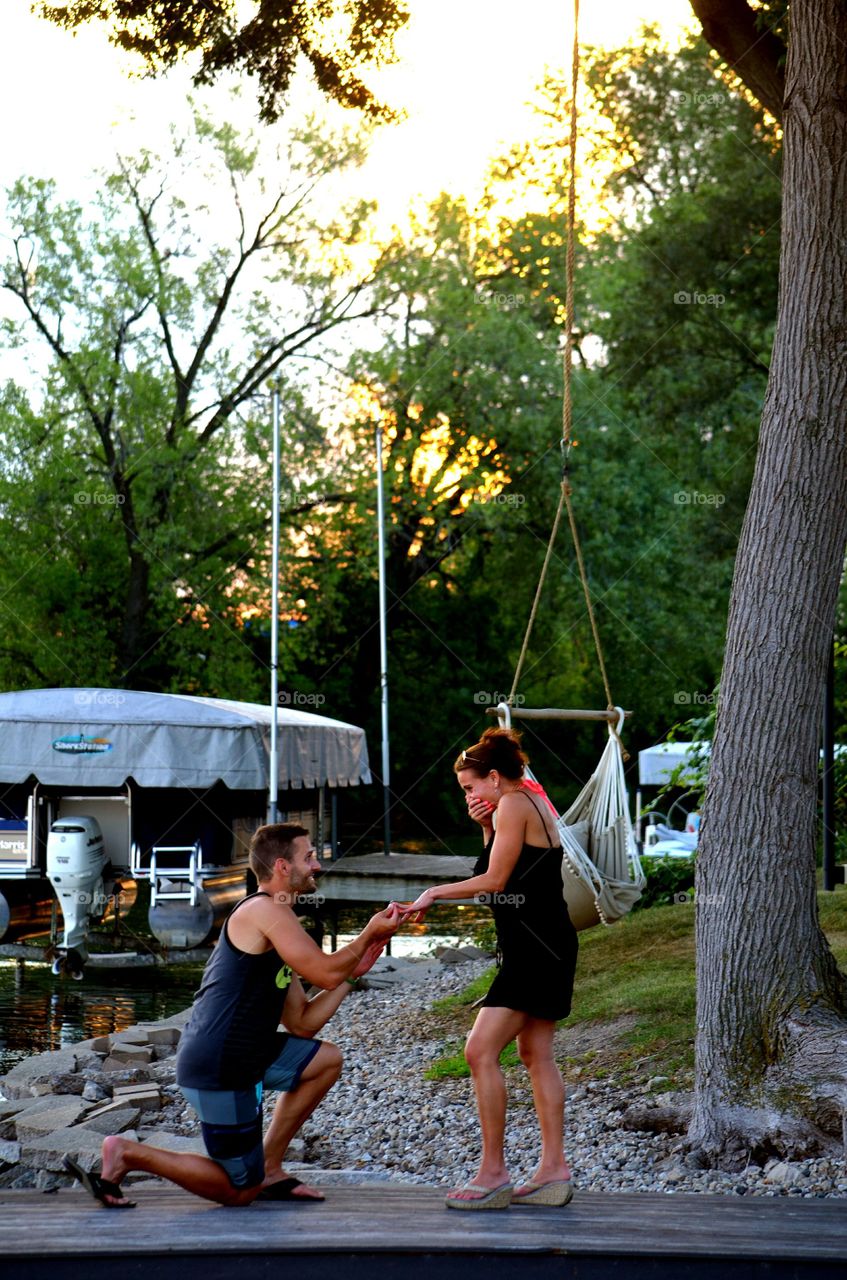 Man proposing woman near tree trunk