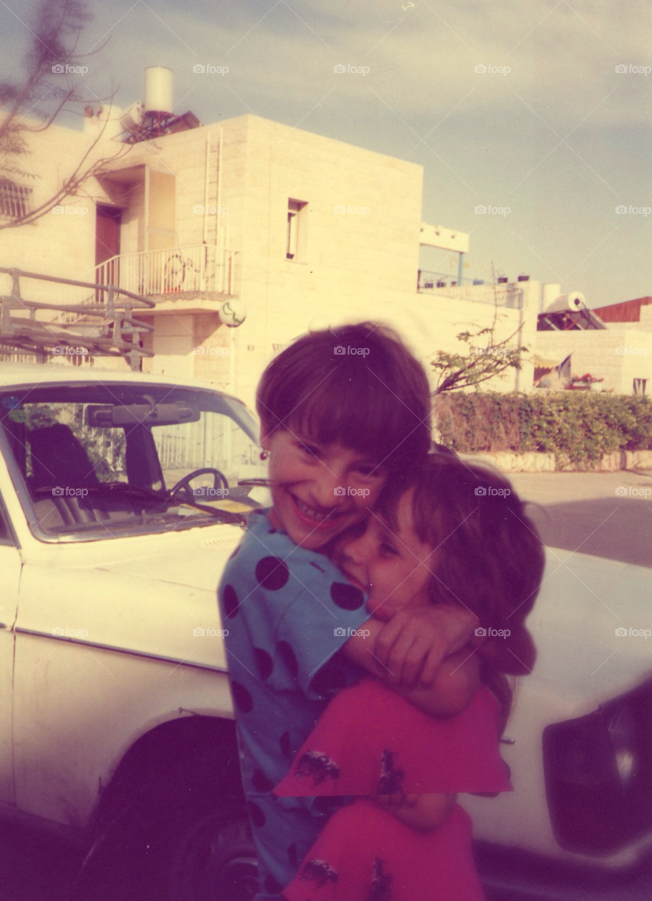 Happy childhood in the 90's . Two girls in the age of 6 or 7 in their neighborhood hugging each other.