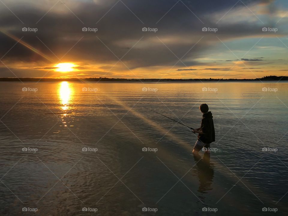 Fishing in the lake at sunset in calm waters. True Canadian fishing. Clouds with orange sunset. Male fishing with his fishing rod. 