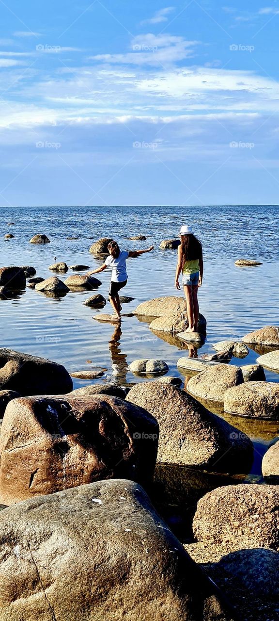 Children jumping on rocks at sea on a sunny summer day