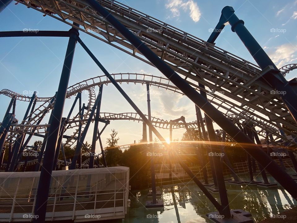 An amusement park comes alive at sunset, with roller coasters twisting gracefully in the sky, illuminated by rows of colorful lights.