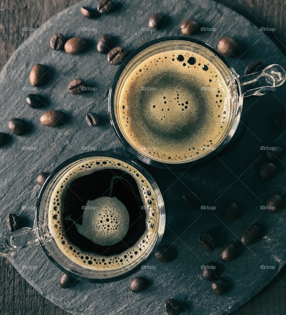 2 glasses of black frothy coffee viewed from above with coffee beans and dark tones