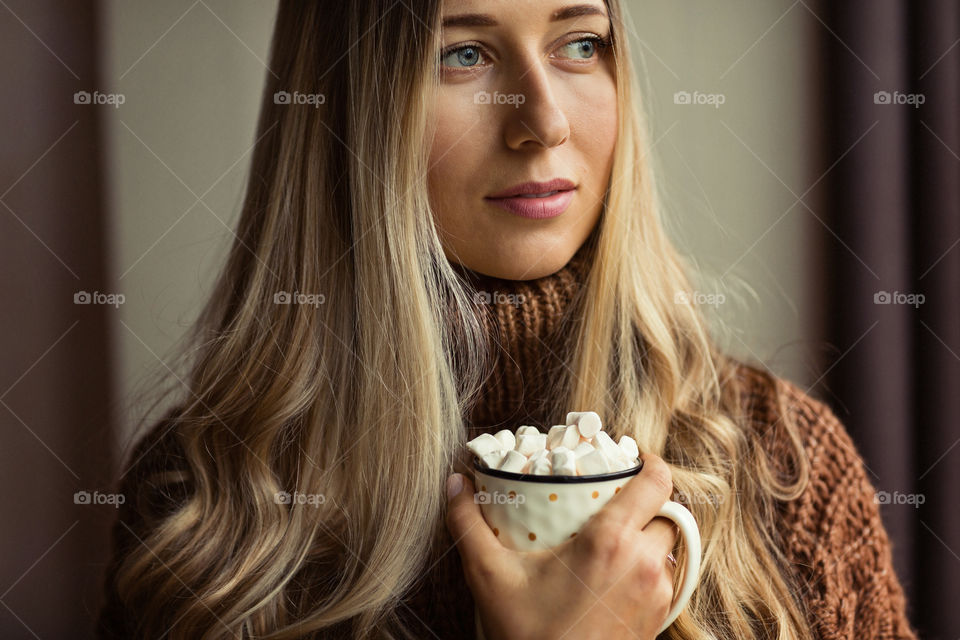 Portrait of beautiful young woman with blonde hair. She holding hand cup of coffee with marshmallow 