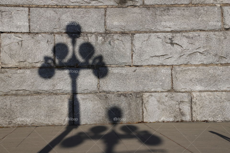 Shadow of lampposts falling on a stone wall 