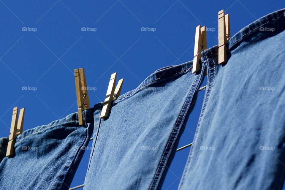 Freshly laundered blue jeans hanging on a clothesline in the sunshine against a blue sky