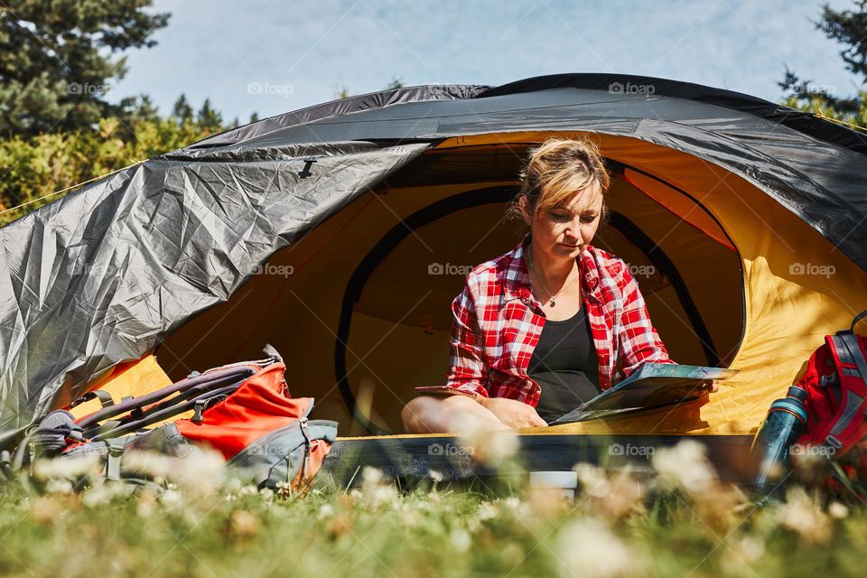 Woman planning next trip while sitting with map in tent. Woman relaxing in tent at camping during summer vacation. Actively spending vacations outdoors close to nature. Concept of camp life