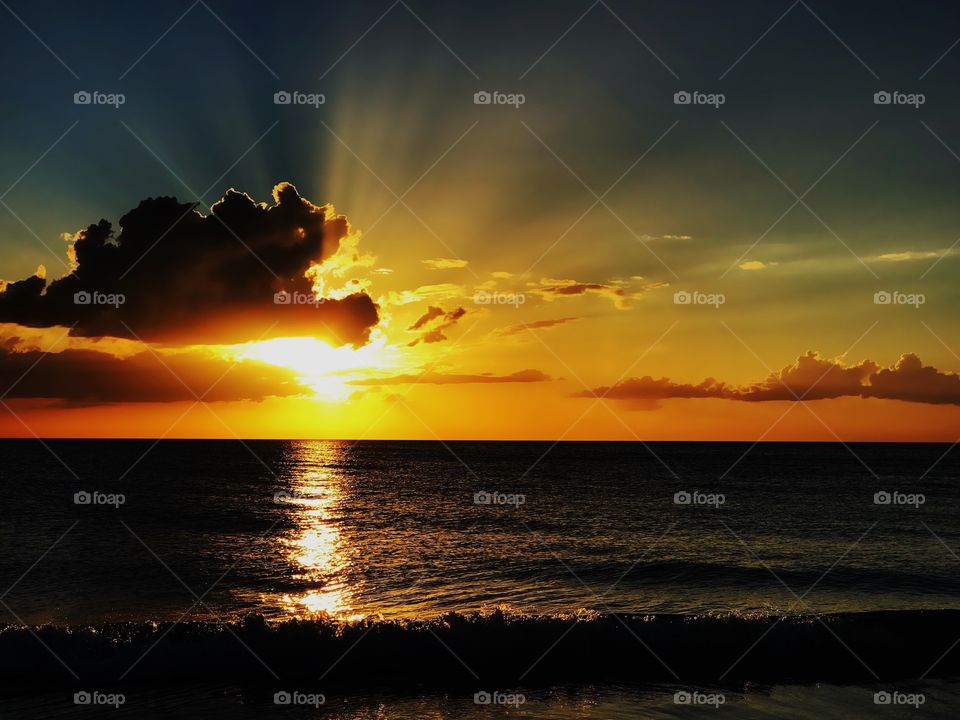 Beautiful dark clouds and golden sun rays merge together into a dazzling ocean sunset.