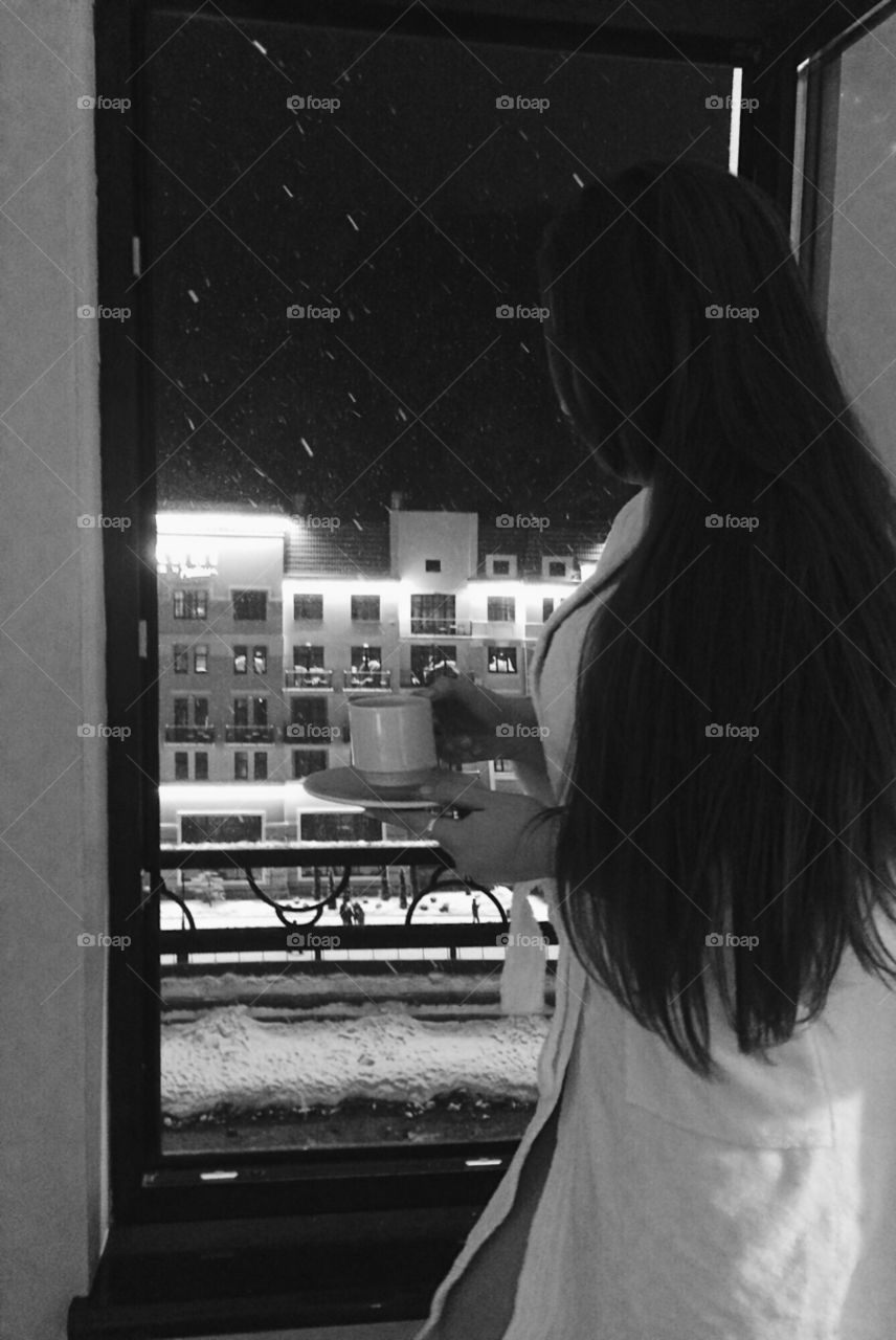 Woman in bathrobe with coffee cup standing in front of glass window