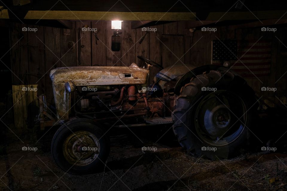 A 1953 Ford Jubilee vintage tractor that is still operational under the dim light of a lantern in an old barn. 