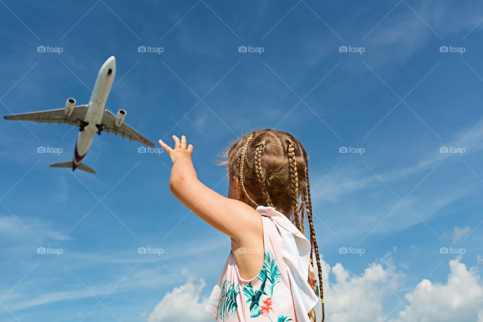 Little girl with blonde braided hair looks to aircraft in blue sky