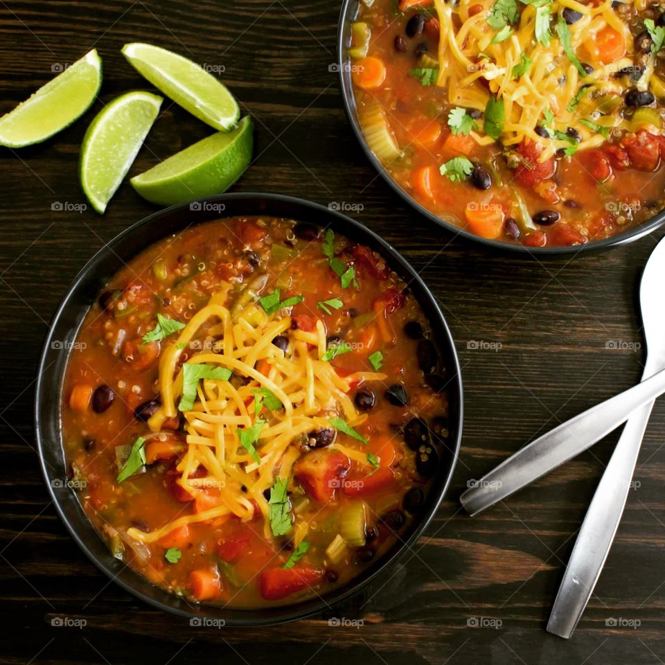 Bowls of Mexican vegetable and quinoa stew garnished with shredded cheese and lime wedges