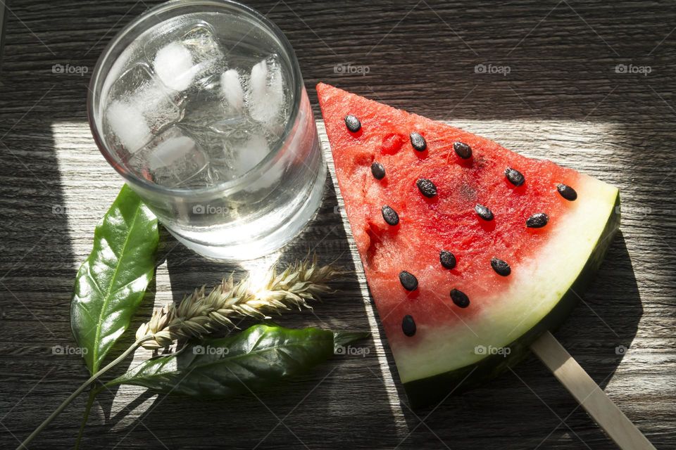 Cold, transparent drink with ice in a glass glass with summer snacks on a wooden background.