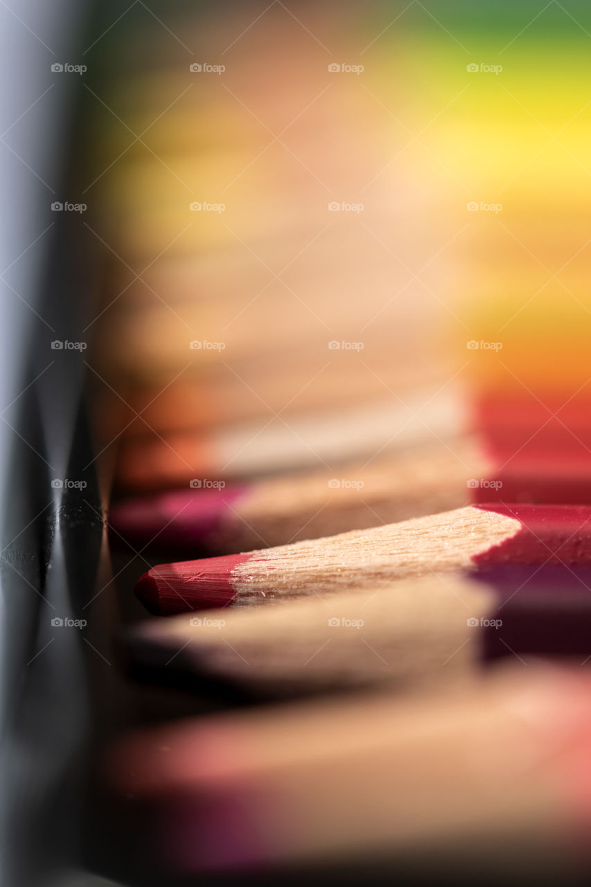 A close up portrait of a red colored pencil in a color pencil box next to other colorful pencils.