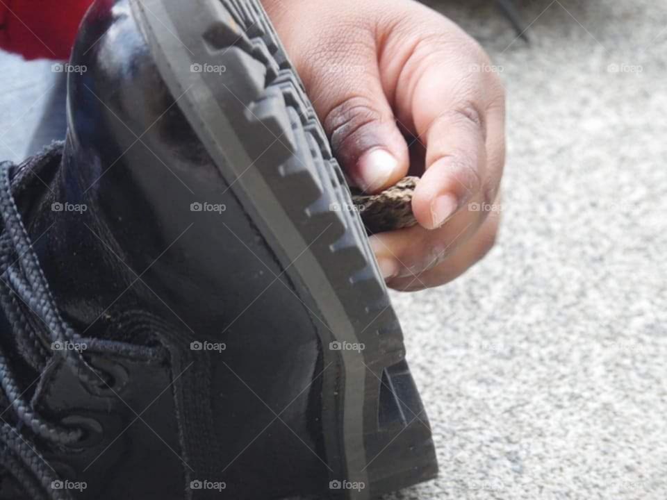 A child's hand playing outdoors with the black rubber on the bottom of his rugged, black, boot.