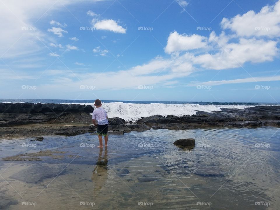 Boy stands in tidal pool and watches waves crash in