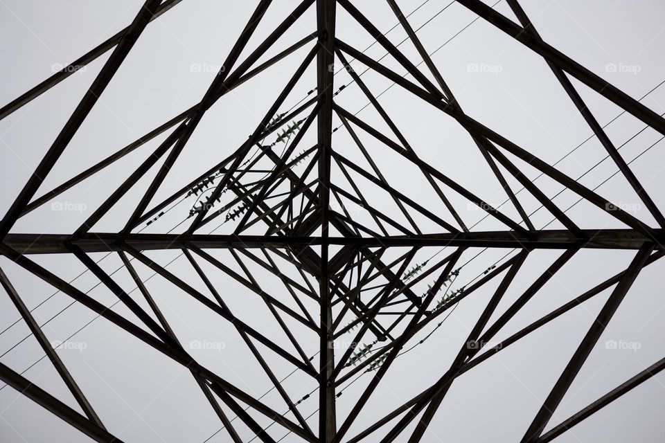 Directly Below Of Electricity Pylon Against Sky. Abstract pattern from bottom view of high voltage pole.