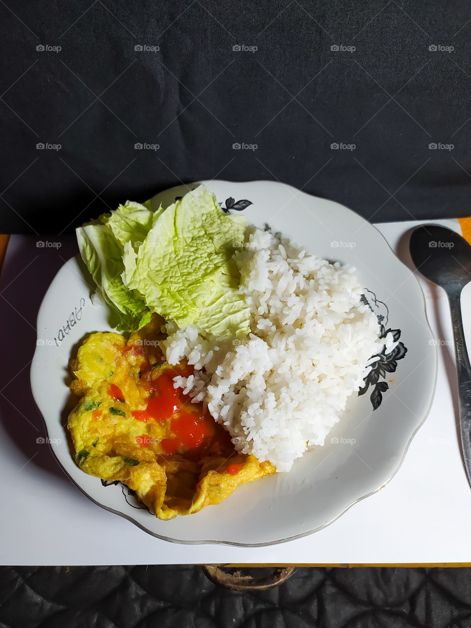 a plate of white rice accompanied by a side dish of fried eggs and fresh vegetables