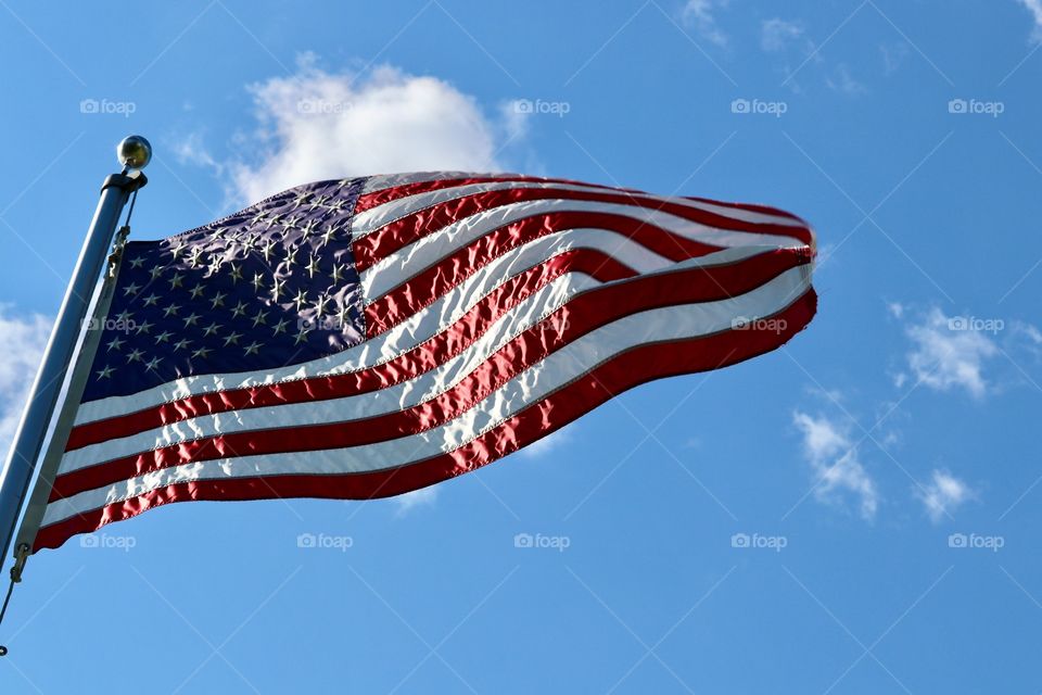 American flag closeup on flagpole flying, rippling in the wind, on vivid clear blue sunny sky closeup