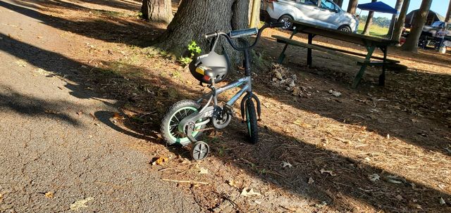 in the shade of a tree is a blue little tike bike with a bike helmet & mint green rims