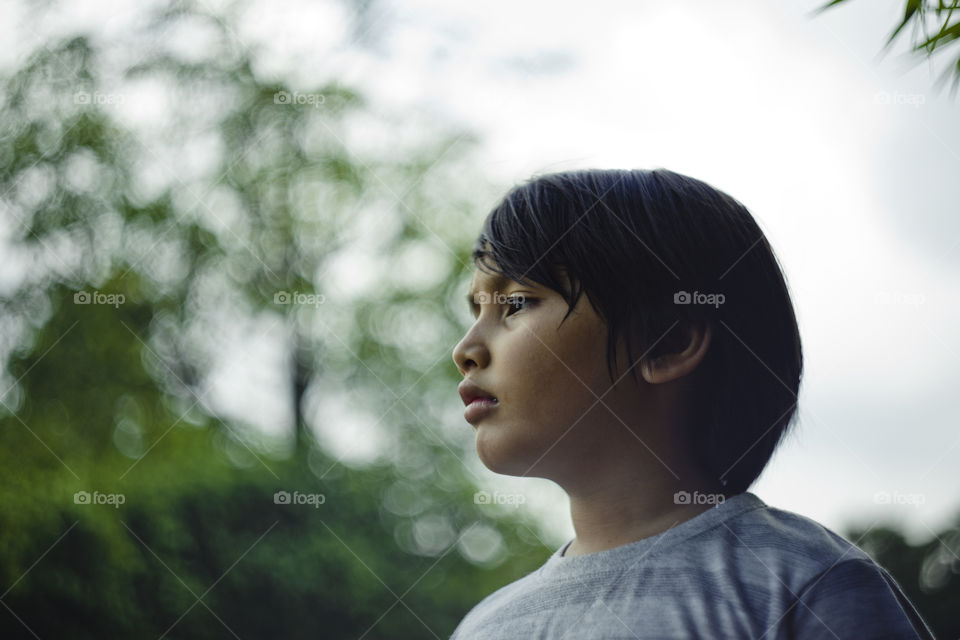 outdoor portrait of young eurasian boy on a blurry out of focus bokeh foliage background