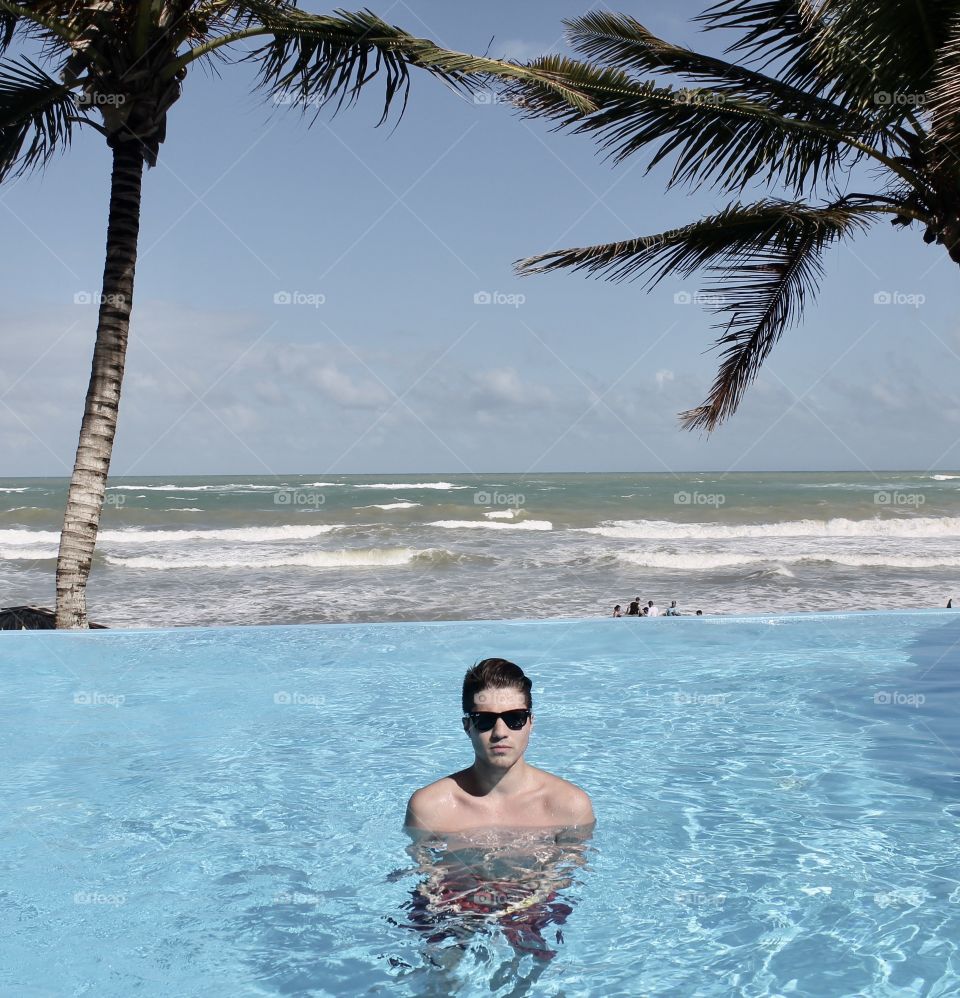 Young shirtless man in infinity pool near sea