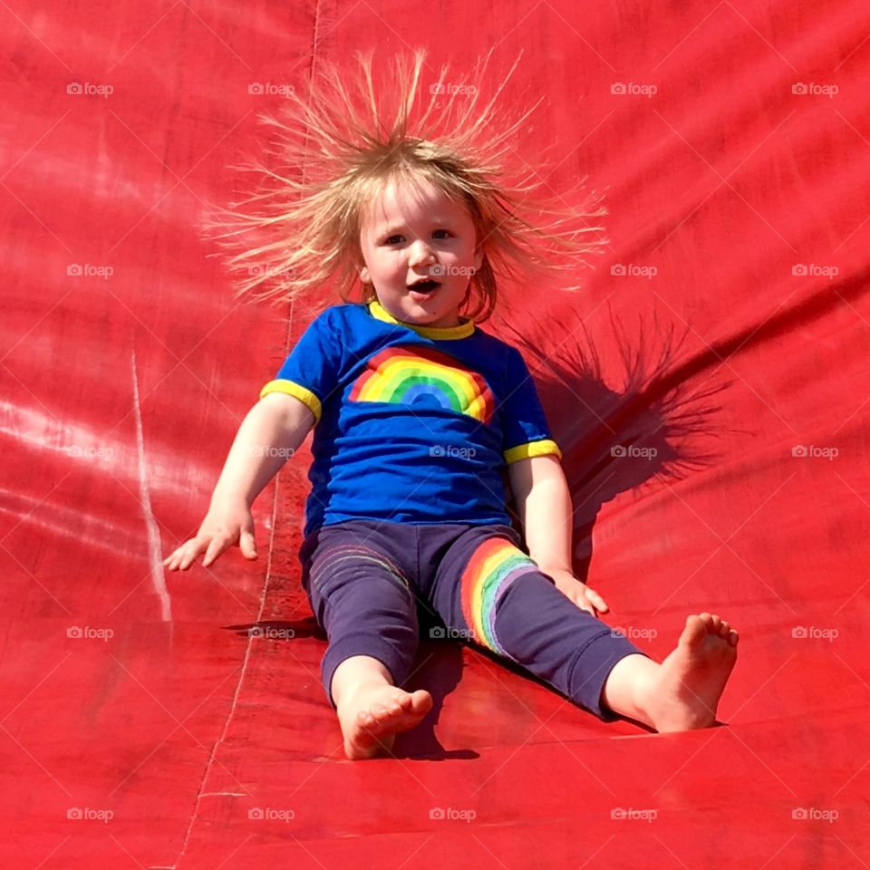 Young child with statically charged hair sliding down an inflatable slide in Ilfracombe, North Devon. 