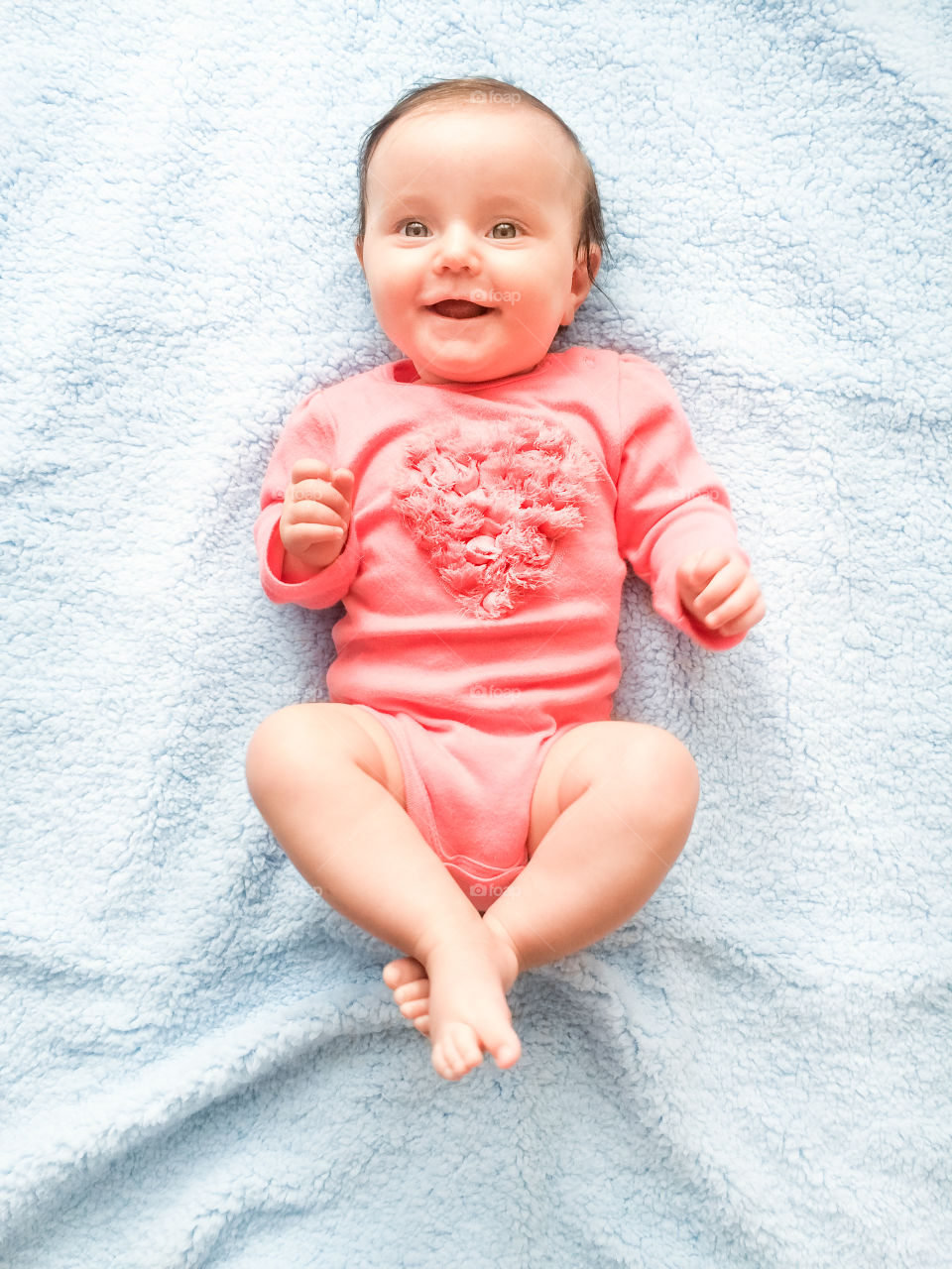 My heart beating. Happy smiling baby girl lying on blanket. She is wearing body suit with heart shape