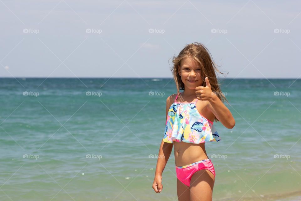 Caucasian girl of 7-8 years in swimming suit looking at camera and showing thumb up