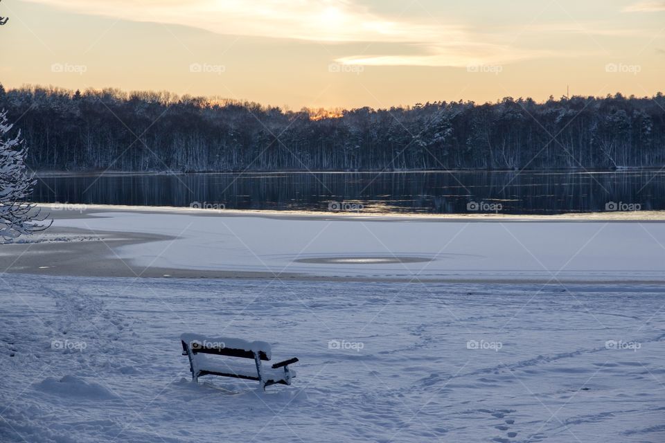Winter wonderland, empty park bench by the lake at sunset - vinter och snö, en tom parkbänk i snöigt vinterlandskap med utsikt över sjö vid solnedgång