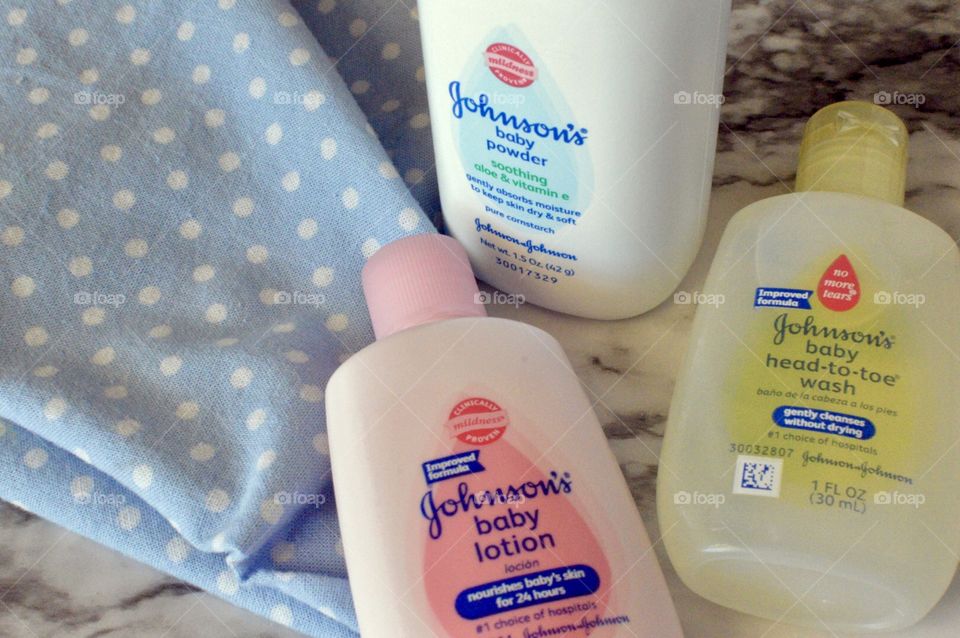 Johnson and Johnson baby powder, lotion, and head to toe body wash on a white marble background with a blue and white polkadot linen