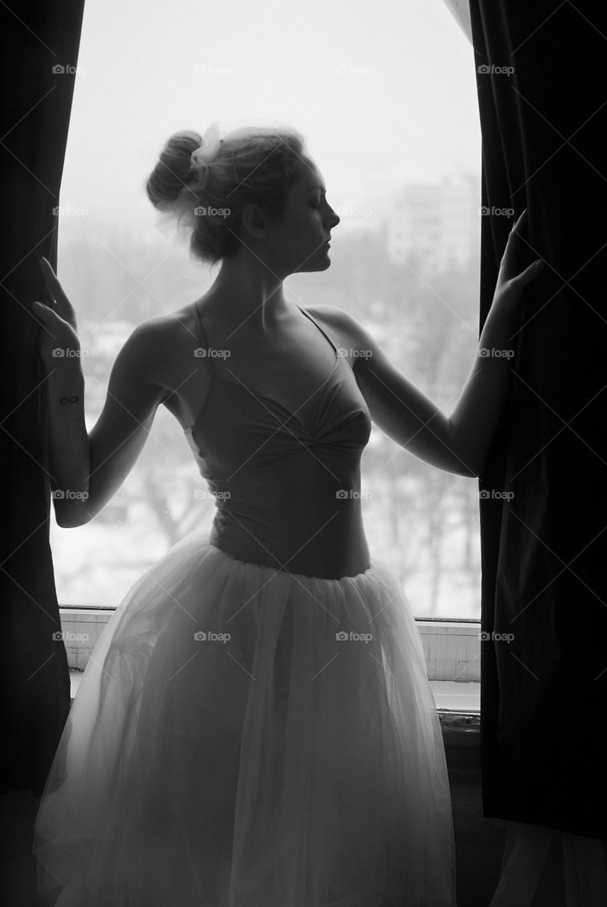 A young and graceful ballerina in pointe shoes and a tutu dances in the studio during the day.