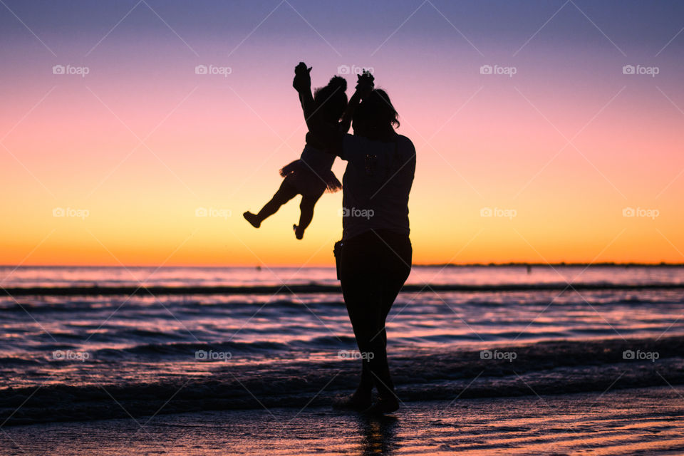 A mom plays with her young daughter on the beach at sunset