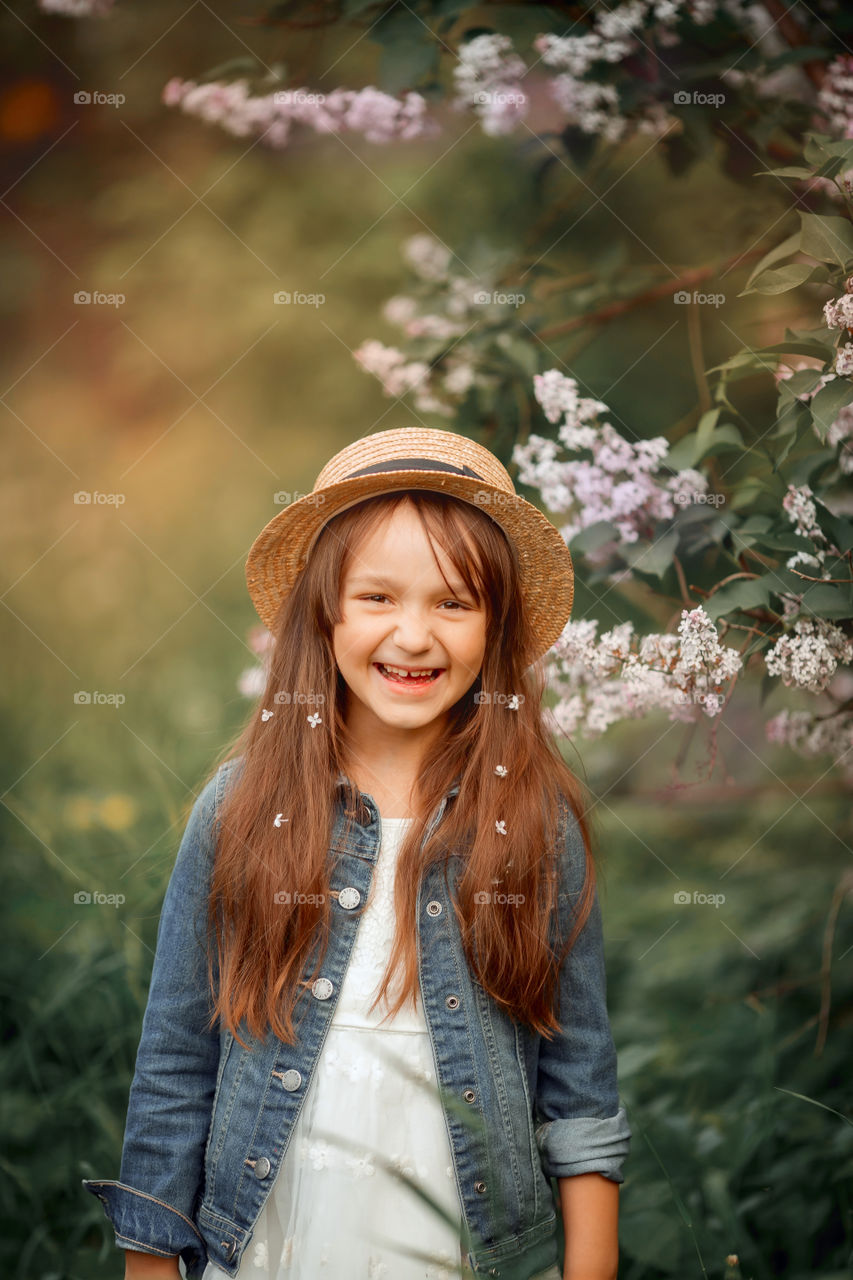 Little girl in a hat near blossom lilac tree at sunset 