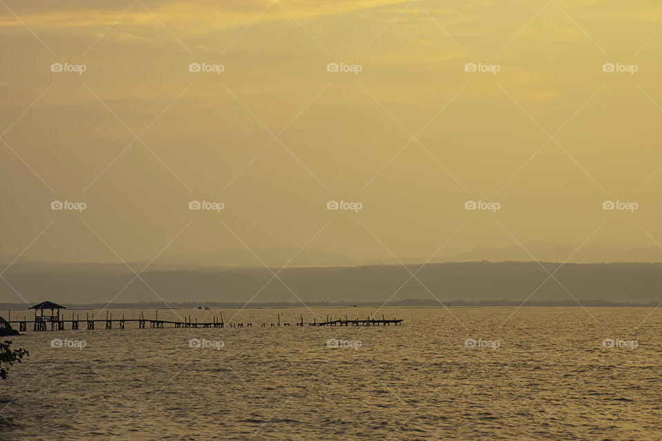 Golden light of sunrise behind the mountains in the sea and the shadow of the wooden bridge at  Trat in Thailand.