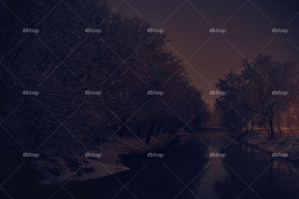 A shot of a calm river surrounded by snow at night.