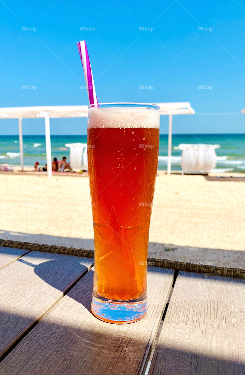 A glass of beer on a table in a beach cafe.  Beach and sea in the background.