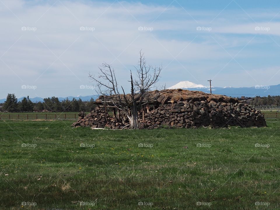 An old homesteading cold storage building built from rocks in the field with mountains in the background on a sunny spring morning. 