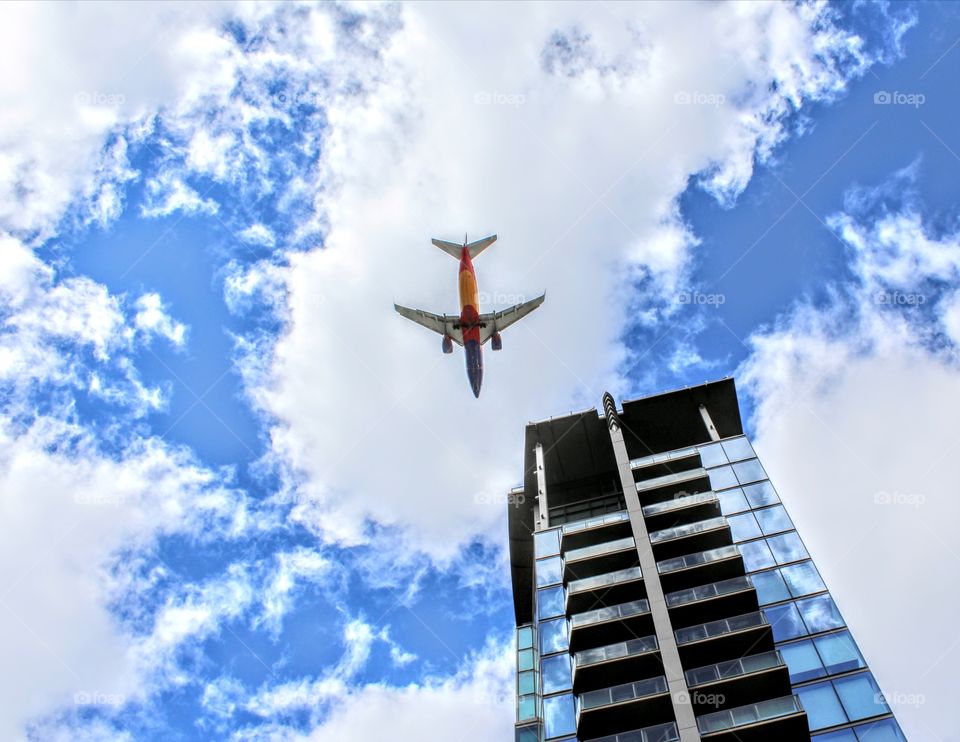 a airplane flying low over a high-rise apartment building in the blue cloudy skys