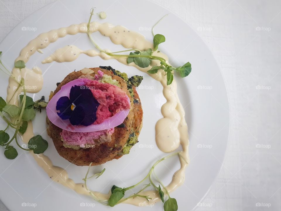 close up of plated fancy resturant meal served salmon hash stack with microgreens and sauce and beetroot eggs with pansy flower