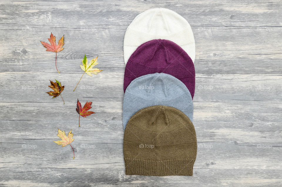 Flat lay of a row of knit beanie hats next to a row of fall leaves