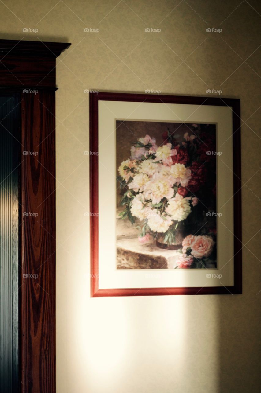 Sunlight streaming onto a watercolor print in a dark mahogany frame on a yellow-patterned, wallpapered wall and dark woodwork (circa 1915)