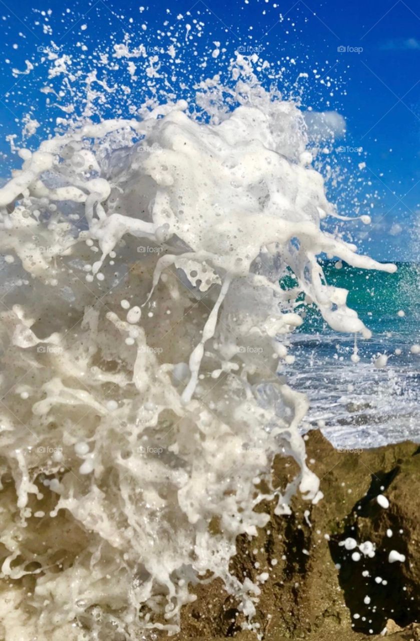 A close up of a wave splashing against rocks with details of sea foam