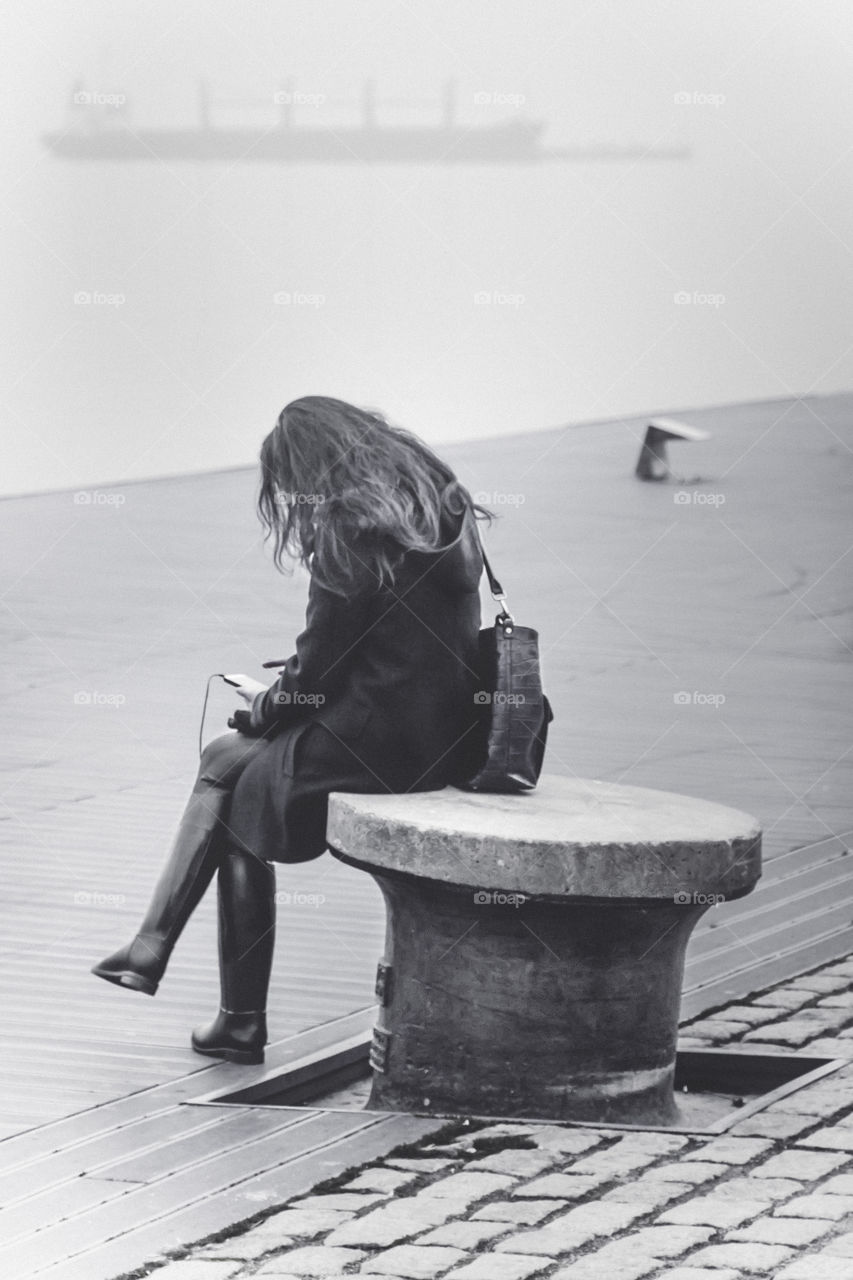 Young Woman Sitting Alone At The Dock Using Her Smartphone And Listening Music
